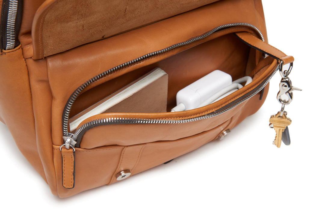 Tan Handcrafted with full grain American leather Padded backpack shoulder straps Roomy interior and front pocket Keychain attachment Interior organizer panel Fits up to a 15" laptop  Strap designed for easy carry on telescoping luggage handles Handcrafted with care in our own factory Natural leather lining Dimensions: 17" x 7" x 12" #color_tan